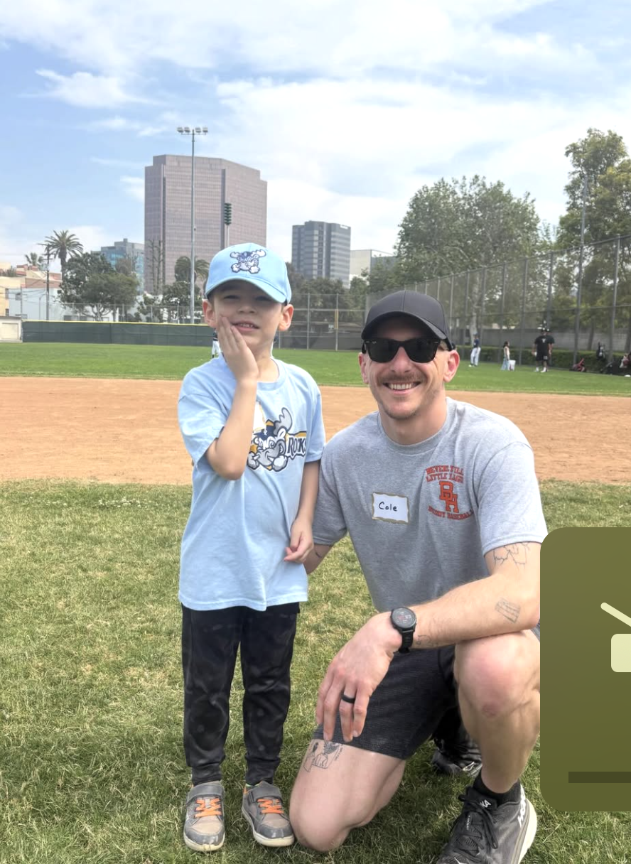 A buddy volunteer kneeling beside a young Rocks player on the infield